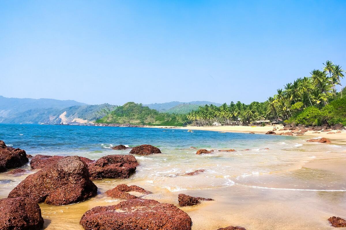 Red rocks and golden sand on a beach in Goa, with palm-covered hills behind