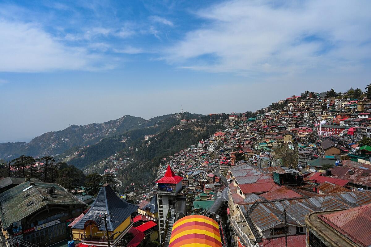Shimla's houses spread across forested ridges under a blue sky