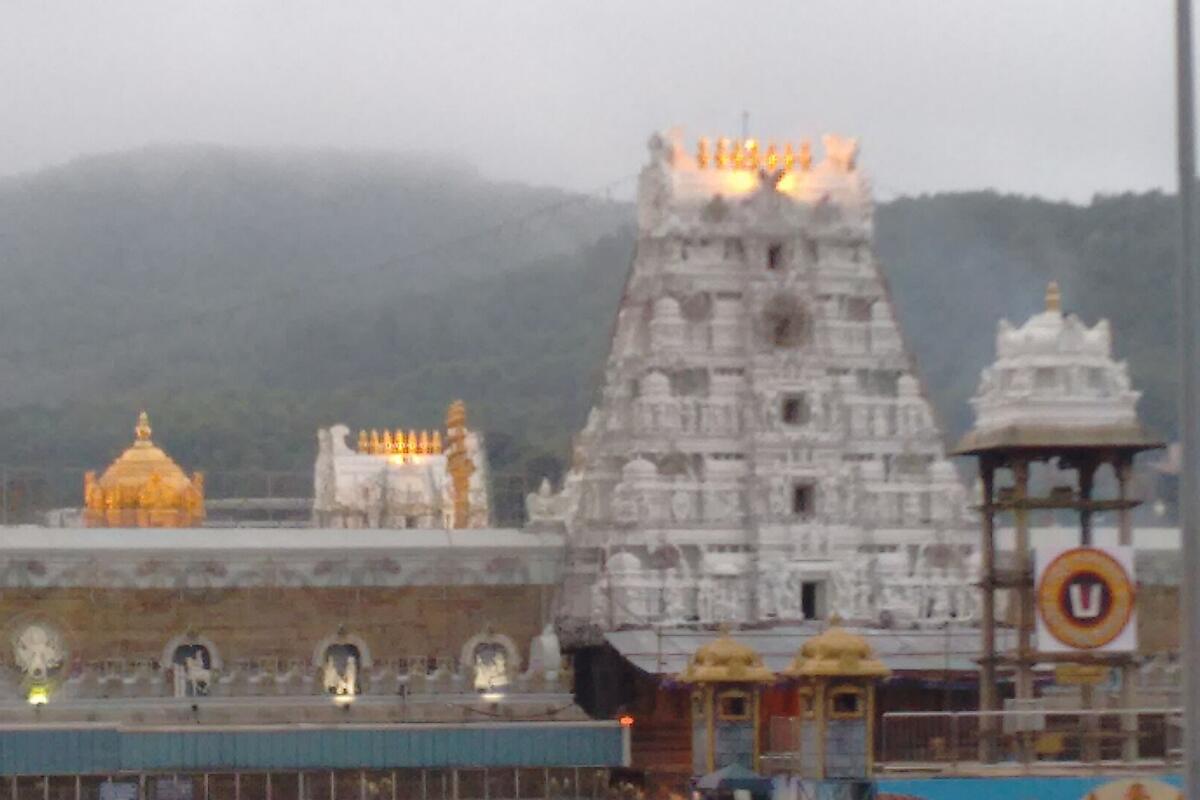 The ornate gopuram of the Tirumala temple with the hills and mist behind