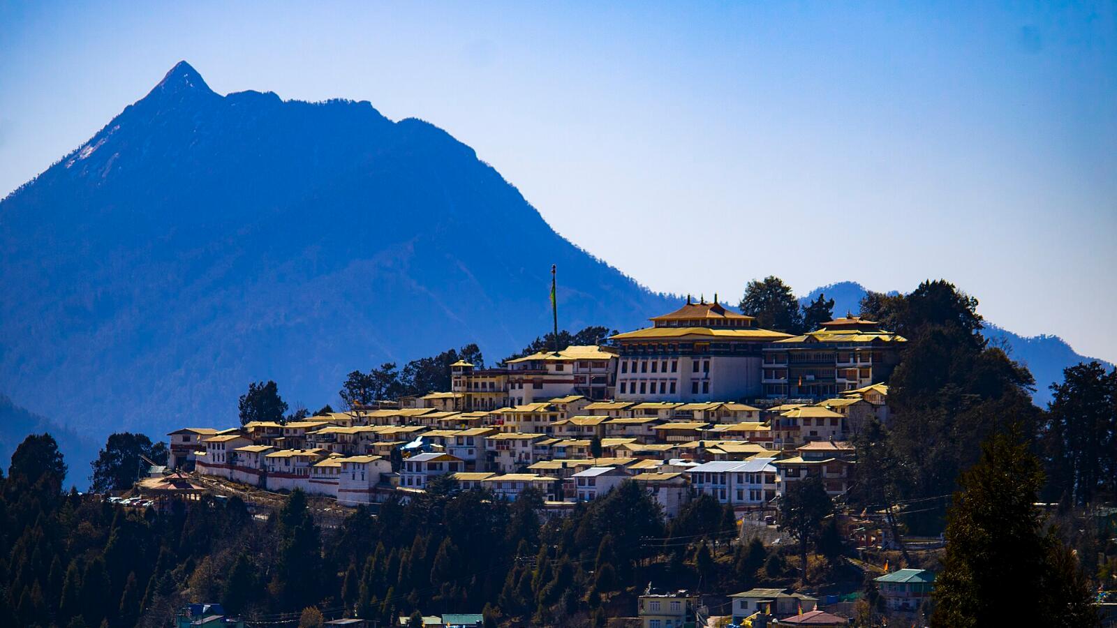 Tawang Monastery spread across a hillside below a tall mountain under a clear blue sky